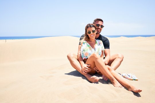Young beautiful couple smiling happy and confident. Sitting with smile on face hugging at the beach