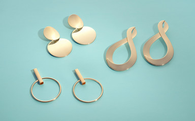 Top view of Three pairs of modern golden earrings on mint green background