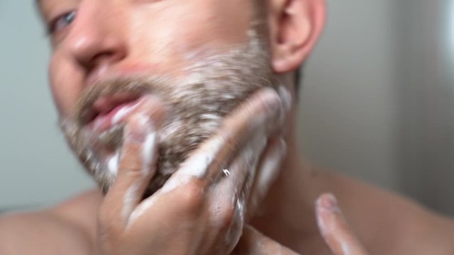 Professional barber man washing his unshaved beard before cutting with electric trimmer. Soaping beard, shampoo foam and special technics in shaving beard at home. Skincare and beard grooming concept