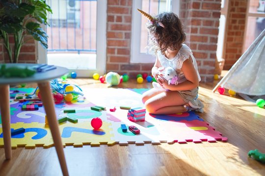 Beautiful toddler wearing glasses and unicorn diadem sitting playing with wooden building blocks at kindergarten