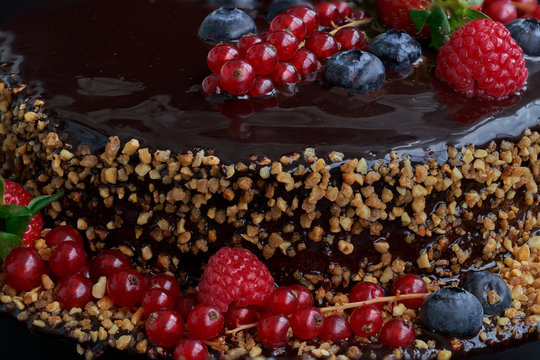 Partail view. Homemade Chocolate Cake. Chocolate bavaroise with chocolate topping. Garnished with red currants, strawberries, blueberries and chopped and toasted almonds. Dark background.