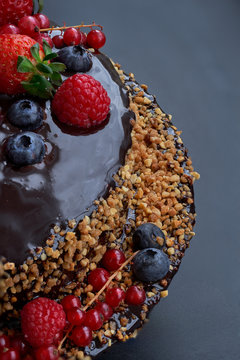 Partail view. Homemade Chocolate Cake. Chocolate bavaroise with chocolate topping. Garnished with red currants, strawberries, blueberries and chopped and toasted almonds. Dark background.