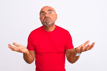 Fototapeta premium Middle age handsome man wearing red casual t-shirt standing over isolated white background clueless and confused expression with arms and hands raised. Doubt concept.