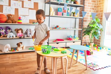Beautiful african american toddler playing with plastic food and cutlery toy at kindergarten