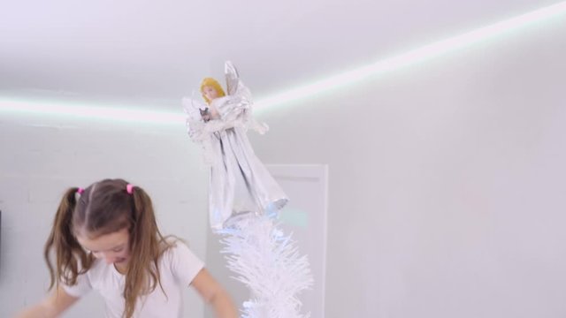 Handsome father holds daughter on shoulders, daughter smiles and put away an angel from the top of Christmas tree.