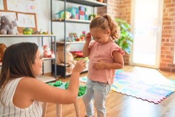 Beautiful teacher and blond student toddler girl playing with plastic frogs toys at kindergarten