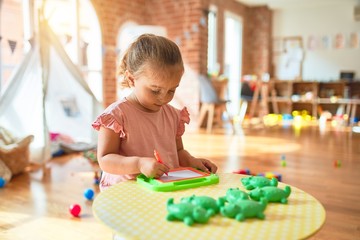 Beautiful blond toddler girl drawing using digital board at kindergarten