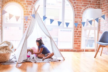 Beautiful toddler girl sitting on the floor playing with unicorn and doll inside  tipi at kindergarten