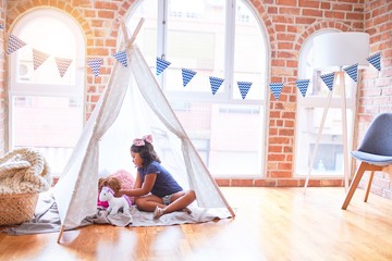 Beautiful toddler girl sitting on the floor playing with unicorn and doll inside  tipi at...