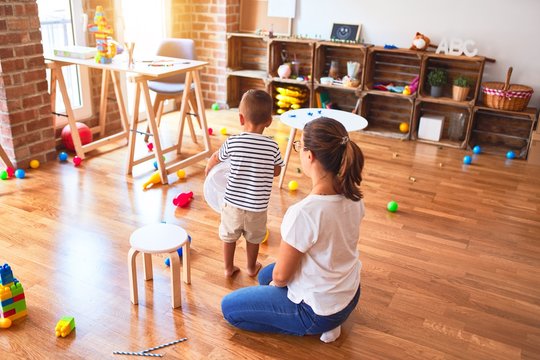 Beautiful teacher and toddler boy playing with plastic basket at kindergarten