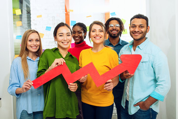 Young happy and colorful business team hold a red statistical arrow. Concept of growing, succesful...