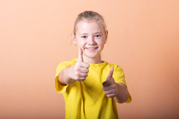 Girl showing thumbs up, on a light orange background.