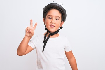 Beautiful kid boy wearing bike security helmet standing over isolated white background smiling with happy face winking at the camera doing victory sign. Number two.