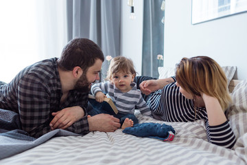 Young couple playing with their 8-month-old baby in bed.