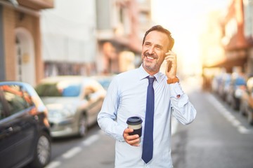 Middle age handsome businessman talking on the smartphone drinking take away coffee smiling