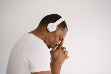 Portrait of a smiling african american man listening to music on headphones thinking. Isolated...