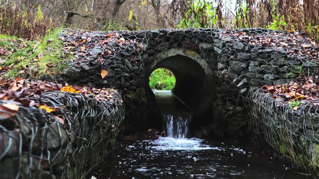 Small brook flowing through concrete pipe in the park