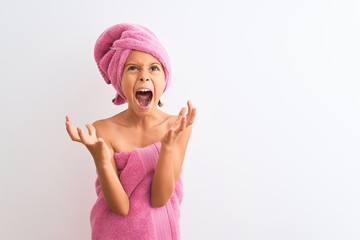 Beautiful child girl wearing shower towel after bath standing over isolated white background crazy and mad shouting and yelling with aggressive expression and arms raised. Frustration concept.