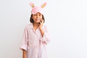 Beautiful child girl wearing sleep mask and pajama standing over isolated white background touching mouth with hand with painful expression because of toothache or dental illness on teeth. 