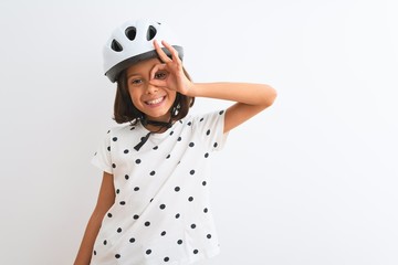 Beautiful child girl wearing security bike helmet standing over isolated white background doing ok gesture with hand smiling, eye looking through fingers with happy face.