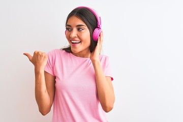 Obraz na płótnie Canvas Young beautiful woman listening to music using headphones over isolated white background pointing and showing with thumb up to the side with happy face smiling