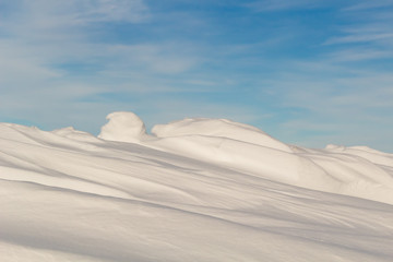 Fototapeta na wymiar A snowdrift against the blue sky and wispy clouds