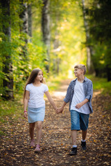 Naklejka na ściany i meble First love. Little boy and girl holding hands and smiling while walking outdoors in park