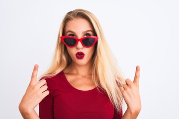 Young beautiful woman wearing red t-shirt and sunglasses over isolated white background amazed and surprised looking up and pointing with fingers and raised arms.
