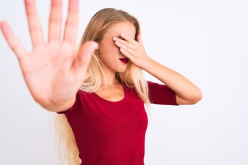 Young beautiful woman wearing red t-shirt standing over isolated white background covering eyes with hands and doing stop gesture with sad and fear expression. Embarrassed and negative concept.