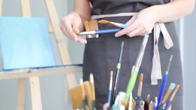 A woman artist in her workshop picks up brushes and selects a brush for painting