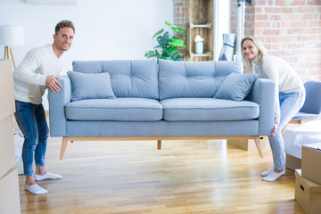 Young beautiful couple moving sofa at new home around cardboard boxes