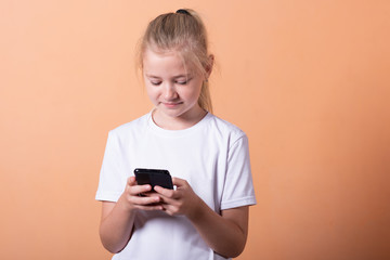 Little girl with a smartphone on a light orange background.