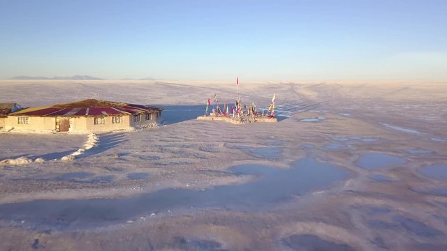 Aerial of flags monument and the first salt hotel in Uyuni salt flat at sunset. DOLLY OUT
