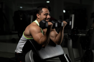 Fototapeta na wymiar Young latin man at gym working biceps extension with dumbbells and pulley 