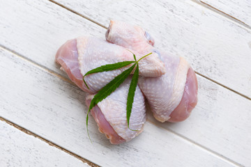 raw chicken legs with herbs marijuana leaf cannabis on wooden table - fresh uncooked chicken meat for cooking