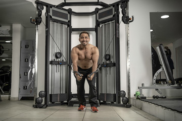 Naklejka premium Young latin man at gym working triceps, chest, back, arms with pulley