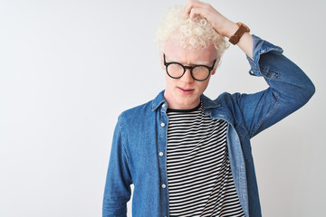 Young albino blond man wearing denim shirt and glasses over isolated white background confuse and...