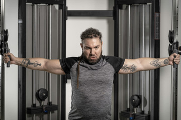 Fototapeta na wymiar Young man in T-shirt at gym with rasta hair working triceps, chest, back, arms with pulley