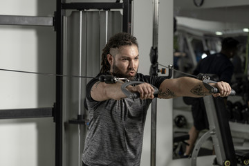 Young man in T-shirt at gym with rasta hair working triceps, chest, back, arms  with pulley