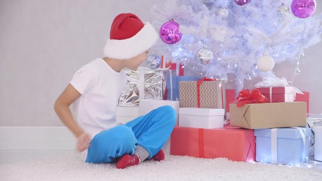 Impatient little boy sneaks to christmas tree at night, when nobody sees and opens a present box, looking inside it fully surprised, then put it back under tree.