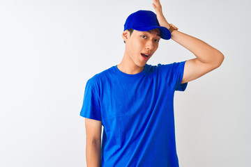Chinese deliveryman wearing blue t-shirt and cap standing over isolated white background surprised with hand on head for mistake, remember error. Forgot, bad memory concept.