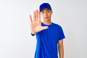 Chinese deliveryman wearing blue t-shirt and cap standing over isolated white background doing stop sing with palm of the hand. Warning expression with negative and serious gesture on the face.