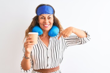 Tourist woman wearing neckpillow sleep mask drinking coffee over isolated white background with surprise face pointing finger to himself