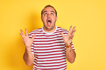 Naklejka premium Young man wearing casual striped t-shirt standing over isolated yellow background celebrating crazy and amazed for success with arms raised and open eyes screaming excited. Winner concept