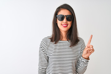 Naklejka premium Chinese woman wearing striped t-shirt and sunglasses standing over isolated white background showing and pointing up with finger number one while smiling confident and happy.
