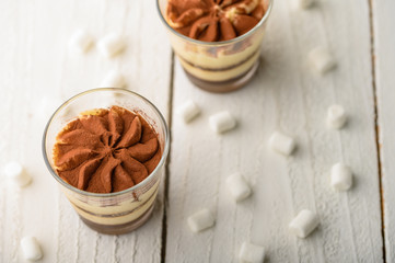 Tiramisu two glasses with marshmallows on a light wooden background