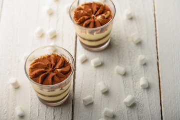 Tiramisu two glasses with marshmallows on a light wooden background