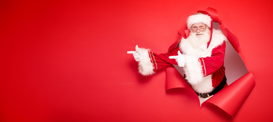 Santa Claus pointing on red empty background.