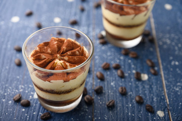 Tiramisu two glasses with coffee grains on a blue wooden background