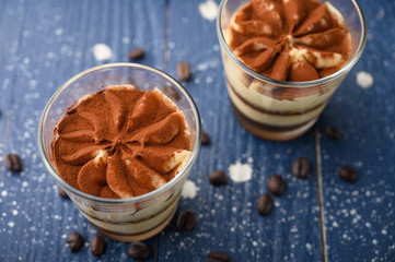 Tiramisu two glasses with coffee grains on a blue wooden background